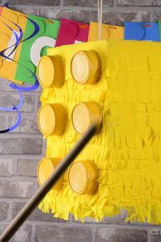 a yellow piece of art hanging from a string on a brick wall with colorful streamers