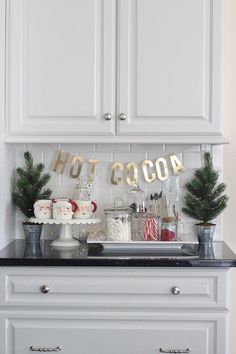 a kitchen with white cabinets and black counter tops, decorated for christmas time in gold lettering