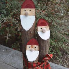 three wooden santa clauss sitting on top of a tree stump in front of some bushes