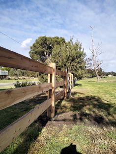 the shadow of a person standing next to a wooden fence in front of a grassy field