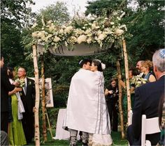 a bride and groom kissing under an arch with white flowers on the grass in front of them