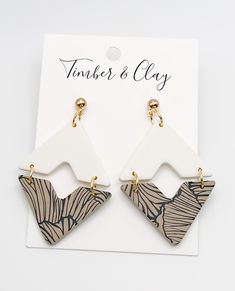 a pair of earrings sitting on top of a piece of white and brown paper next to a card