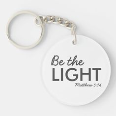 a white keychain with the words be the light written in black on it