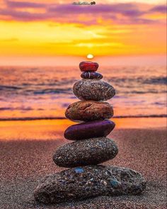 a stack of rocks sitting on top of a beach next to the ocean at sunset