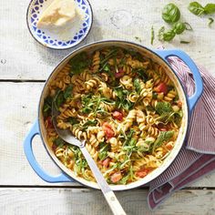 a pot filled with pasta and spinach on top of a wooden table next to a spoon