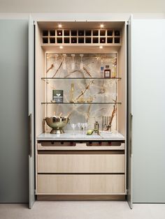 an open cabinet with wine glasses and bottles on the top shelf, in front of a counter