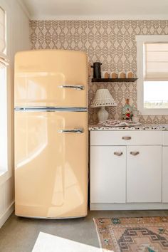 an old - fashioned refrigerator stands in the middle of a kitchen with white cabinets and patterned wallpaper