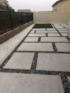 a walkway made out of stones and gravel in front of a fenced in area