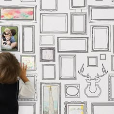 a young boy drawing on a wall with black and white pictures behind him, while another child holds his hand up to their face