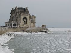 people are standing on the edge of an icy body of water in front of a large building