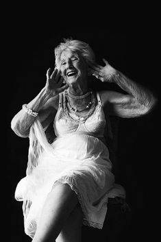 an older woman sitting in a chair with her hands on her head and smiling at the camera