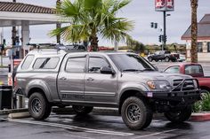 a silver truck parked in a parking lot next to a palm tree and gas station