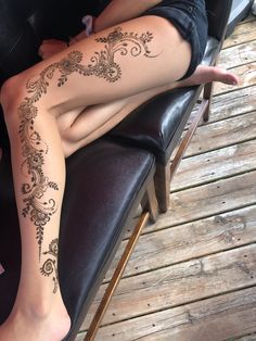 a woman sitting on top of a black chair next to a wooden floor covered in tattoos