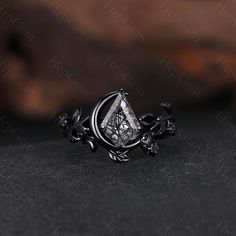 a ring with an intricate design on the front and side, sitting on top of a black surface