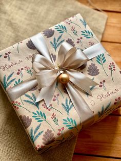 a present wrapped in paper with a bow and ribbon tied around it on top of a wooden table