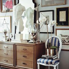 a room with pictures on the wall and a chair in front of a dresser filled with vases