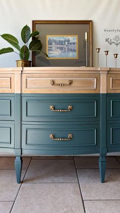 a blue dresser with gold handles and brass knobs on the drawers is shown in front of a framed painting