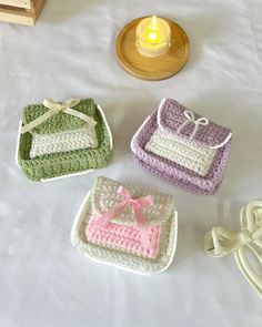 three crocheted purses sitting on top of a white bed next to a candle