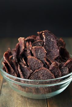 a glass bowl filled with beef strips on top of a wooden table