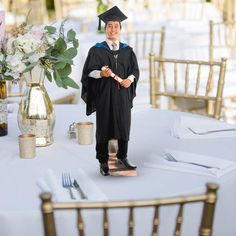 a man in a graduation cap and gown standing next to a table set with flowers