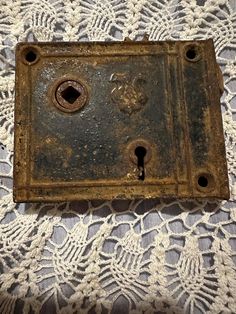 an old metal box on a white lace tablecloth with holes in the middle that are missing