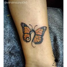 a small butterfly tattoo on the ankle is shown in black and orange colors with swirls