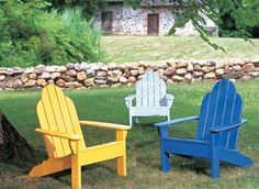 three adironda chairs sitting in the grass next to a tree and stone wall