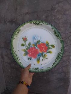 a hand is pointing at a plate with flowers painted on the front and side of it