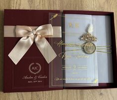 an opened wedding card with a ribbon and brooch on the front, in a gift box