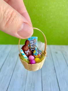 a hand is holding an easter basket filled with eggs and candies on a wooden table