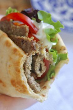 a close up of a person holding a burrito with meat and lettuce