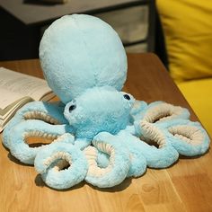 an octopus stuffed animal sitting on top of a wooden table next to a open book