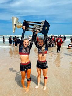 two cheerleaders holding up trophies on the beach