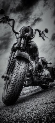 a black and white photo of a motorcycle parked on the side of the road with clouds in the background