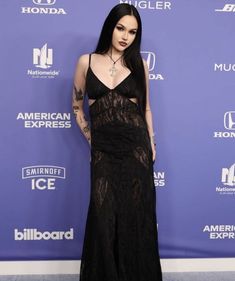 a woman in a black dress standing on a blue carpet with her hands behind her back