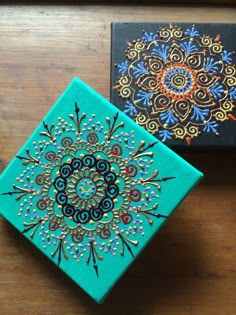 two small boxes with designs on them sitting on a wooden table next to each other