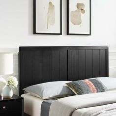 a bed with two framed pictures above it in a white and black bedroom, next to a night stand