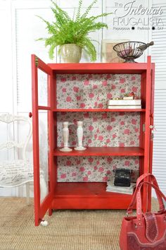 a red bookcase sitting on top of a rug next to a vase and purse