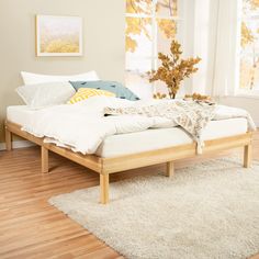 a bed sitting on top of a hard wood floor next to a window with white curtains