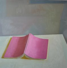 an open pink book sitting on top of a white table next to a yellow cup