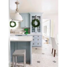 a white and blue kitchen with wreaths on the cabinet doors, an island countertop and stools