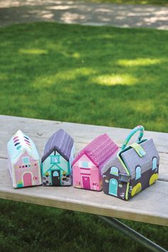 three little houses are sitting on a bench in the grass, one is pink and one is blue