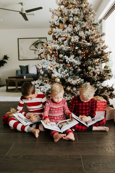 two children sitting in front of a christmas tree reading books