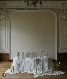 the table is covered with white cloths and flowers in front of an ornate wall