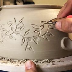 a person is working on a vase with flowers and leaves painted on it's sides