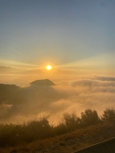 the sun is setting over some hills covered in fog