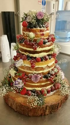 a multi layer cake sitting on top of a wooden table covered in flowers and berries