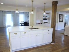 an open kitchen with white cabinets and wood flooring, along with hanging lights over the island