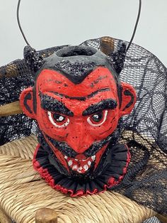 a red devil mask sitting on top of a wicker chair next to a black net