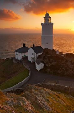 a lighthouse on top of a rocky cliff near the ocean at sunset, with clouds in the sky